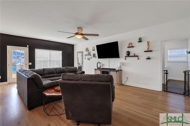 living room with a textured ceiling, light hardwood / wood-style flooring, ceiling fan, and a healthy amount of sunlight