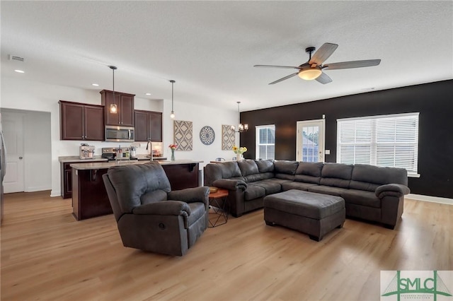 living room with ceiling fan with notable chandelier, a textured ceiling, and light wood-type flooring