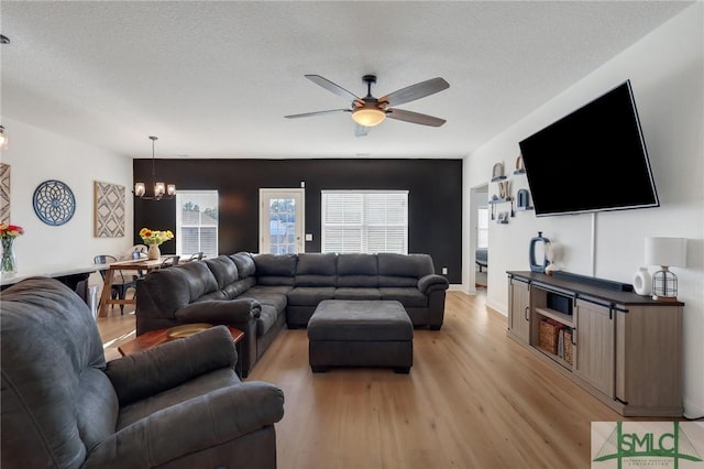 living room featuring ceiling fan with notable chandelier, a textured ceiling, and light hardwood / wood-style flooring