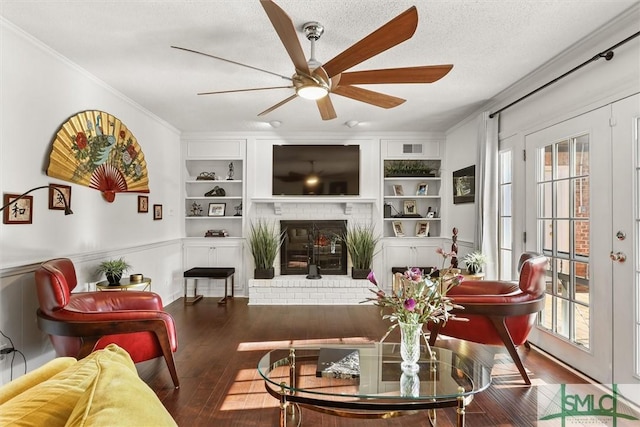 living room with built in shelves, a textured ceiling, crown molding, wood-type flooring, and a fireplace