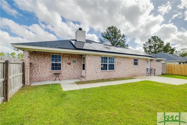 back of property with a yard, a patio, and solar panels