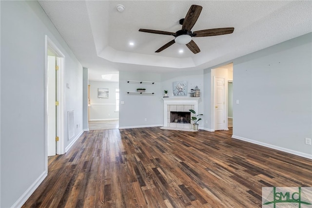 unfurnished living room with a tile fireplace, a raised ceiling, dark hardwood / wood-style floors, ceiling fan, and a textured ceiling