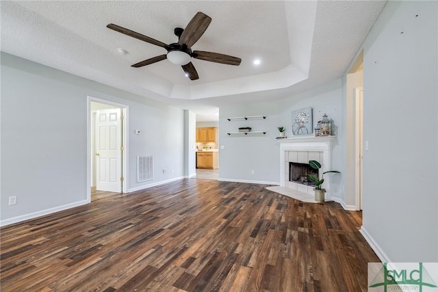 unfurnished living room with a raised ceiling, a tiled fireplace, ceiling fan, and dark hardwood / wood-style floors