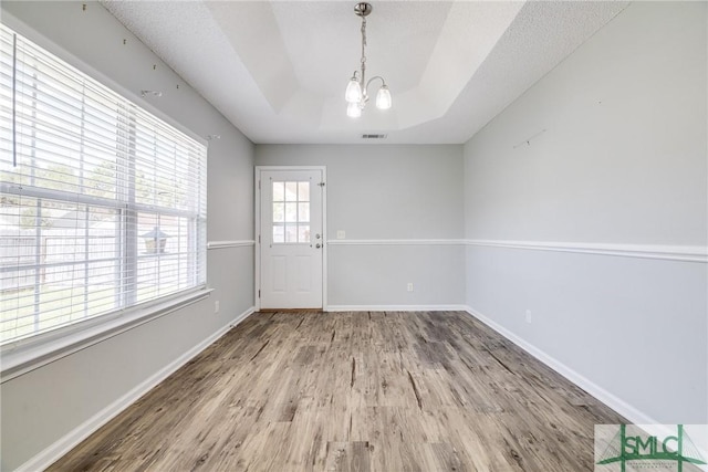 unfurnished dining area featuring a raised ceiling, hardwood / wood-style flooring, and an inviting chandelier