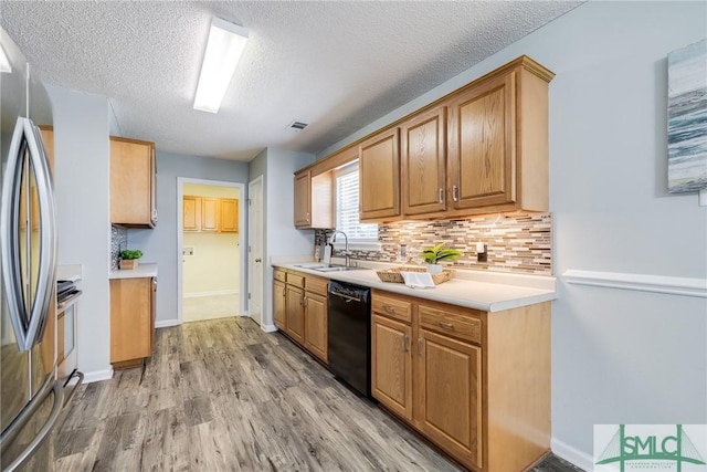 kitchen with sink, decorative backsplash, a textured ceiling, black dishwasher, and stainless steel refrigerator