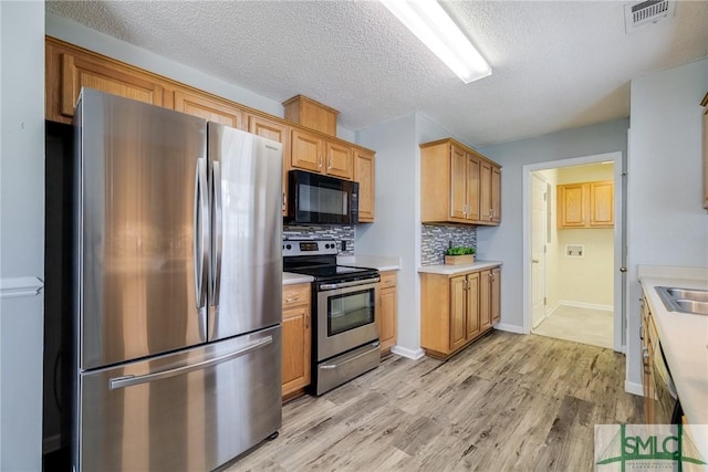 kitchen featuring appliances with stainless steel finishes, light wood-type flooring, tasteful backsplash, a textured ceiling, and sink