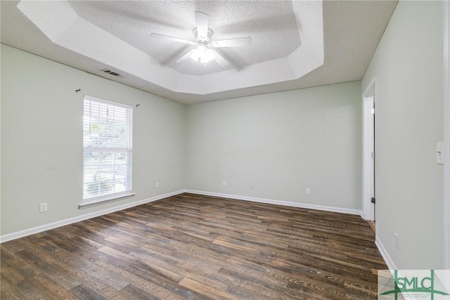 empty room featuring ceiling fan, dark hardwood / wood-style floors, a raised ceiling, and a textured ceiling