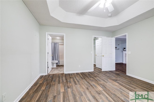 unfurnished bedroom with ceiling fan, a spacious closet, connected bathroom, and a tray ceiling