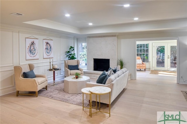 living room featuring a large fireplace, a raised ceiling, crown molding, and a wealth of natural light