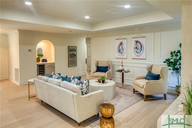 living room featuring light wood-type flooring, ornamental molding, wine cooler, and a tray ceiling