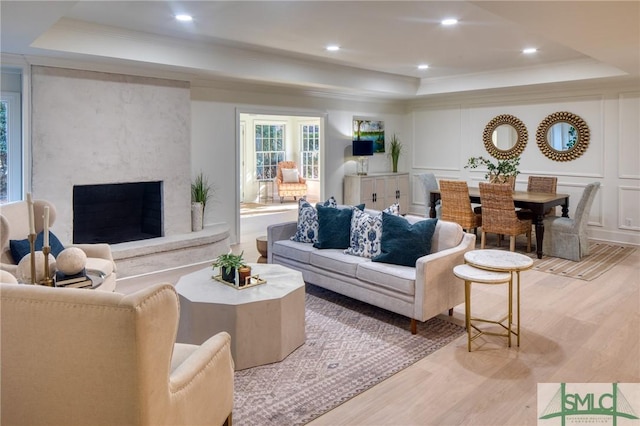 living room featuring a tray ceiling, a fireplace, light hardwood / wood-style flooring, and ornamental molding