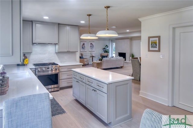 kitchen with a large fireplace, high end stainless steel range oven, decorative light fixtures, light hardwood / wood-style flooring, and gray cabinets