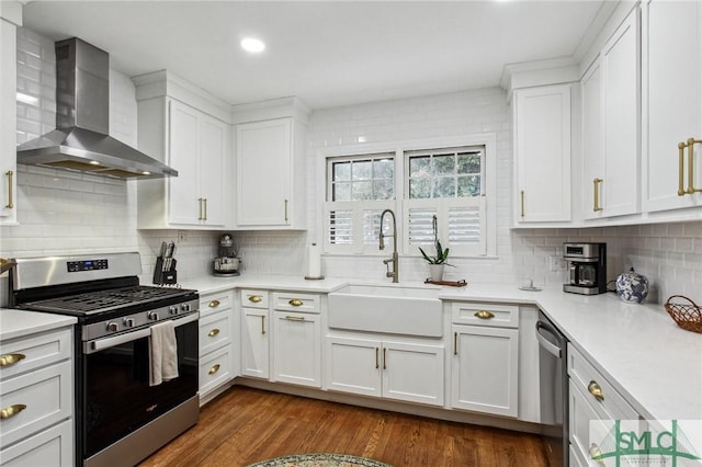 kitchen featuring white cabinets, wall chimney range hood, sink, and appliances with stainless steel finishes