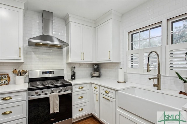 kitchen with gas stove, white cabinetry, sink, and wall chimney range hood