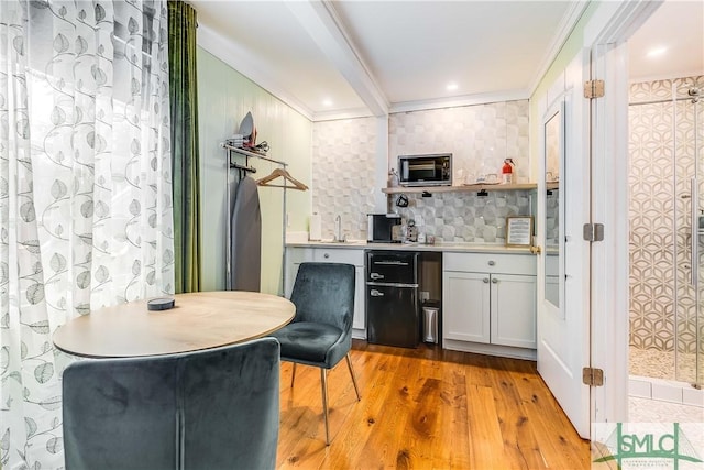 bar featuring light wood-type flooring, tasteful backsplash, ornamental molding, sink, and white cabinetry