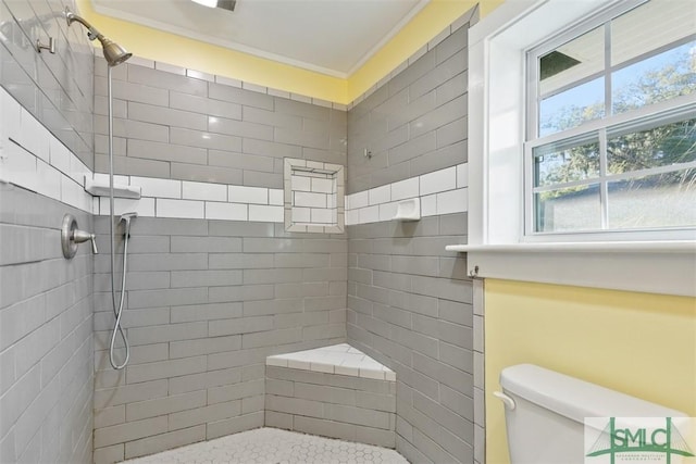 bathroom with toilet, crown molding, and tiled shower