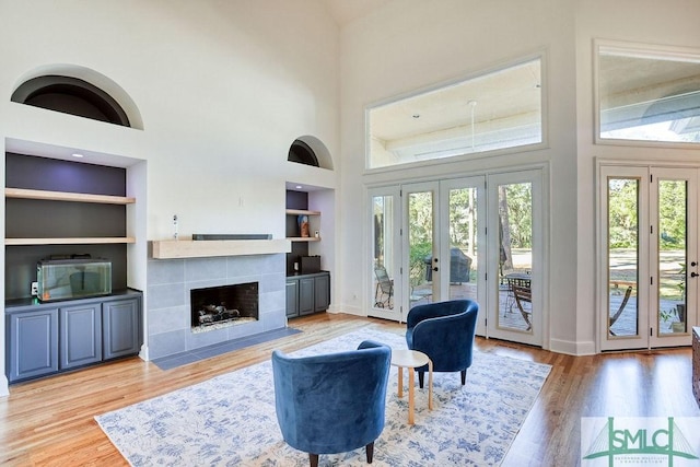 living room featuring a tile fireplace, french doors, a high ceiling, built in features, and light hardwood / wood-style flooring