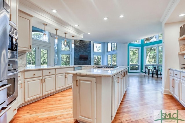 kitchen with kitchen peninsula, appliances with stainless steel finishes, light wood-type flooring, decorative light fixtures, and a center island