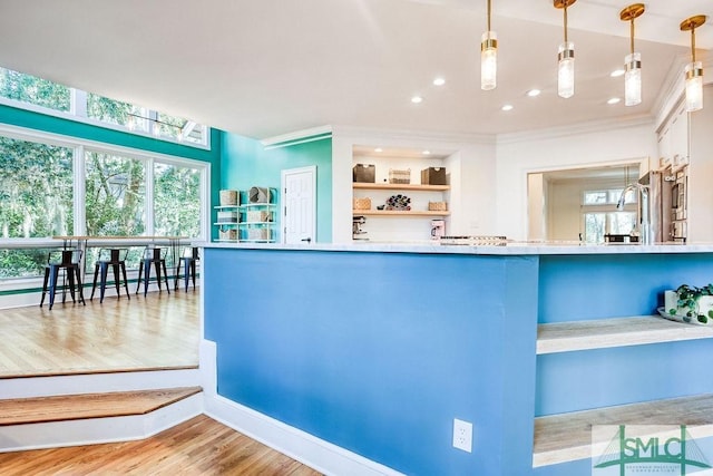 kitchen with crown molding, kitchen peninsula, hanging light fixtures, and light hardwood / wood-style flooring