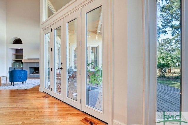 doorway to outside featuring french doors, light wood-type flooring, a wealth of natural light, and a tiled fireplace