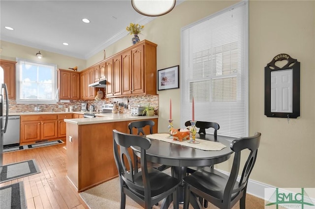 kitchen featuring crown molding, decorative backsplash, light hardwood / wood-style floors, kitchen peninsula, and stainless steel appliances