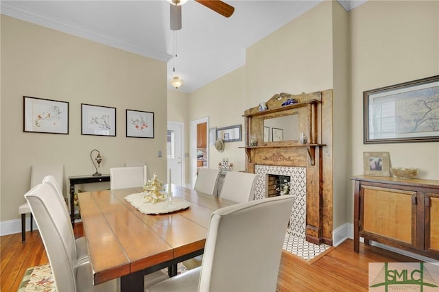 dining space featuring ceiling fan, light wood-type flooring, ornamental molding, and a tile fireplace