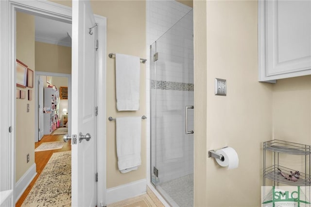 bathroom with ornamental molding, a shower with shower door, and hardwood / wood-style floors