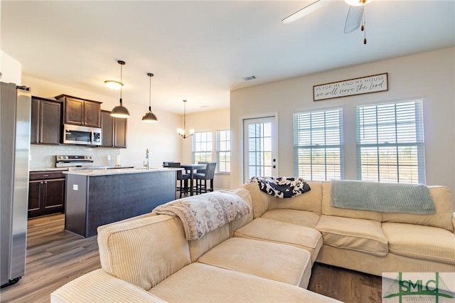 living area with light wood-style flooring, visible vents, and ceiling fan with notable chandelier