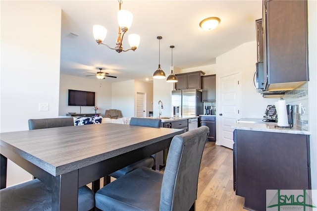 dining space with ceiling fan with notable chandelier, wood finished floors, and visible vents