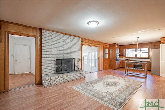 living room featuring wooden walls, light wood-type flooring, and a brick fireplace