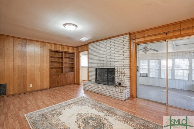 unfurnished living room featuring a brick fireplace, wooden walls, and hardwood / wood-style flooring