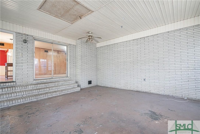 spare room featuring ceiling fan, concrete flooring, and brick wall