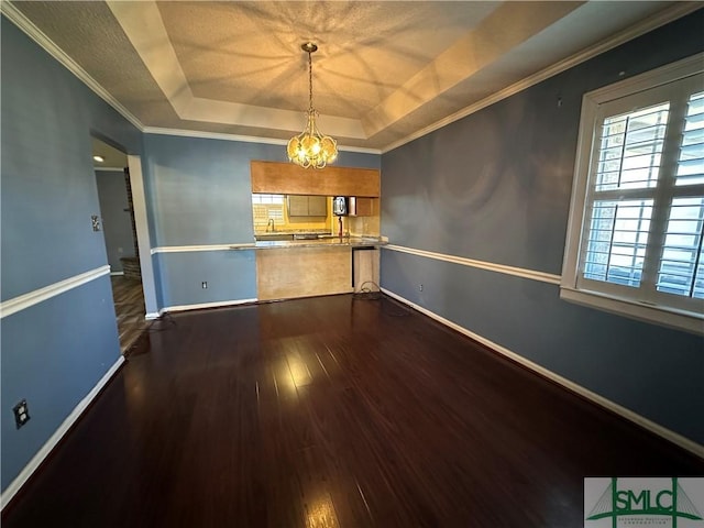 unfurnished dining area with an inviting chandelier, a raised ceiling, sink, ornamental molding, and wood-type flooring