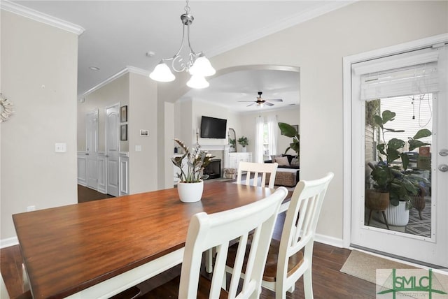 dining room with ceiling fan with notable chandelier, crown molding, and dark wood-type flooring