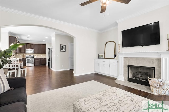 living room featuring a tile fireplace, crown molding, ceiling fan, and dark hardwood / wood-style floors