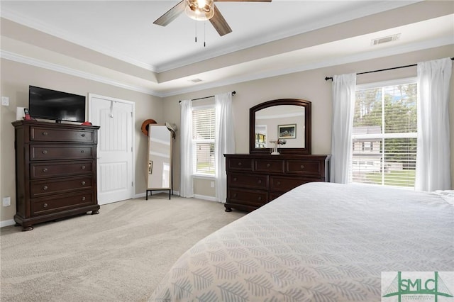 carpeted bedroom with a closet, a tray ceiling, ceiling fan, and crown molding