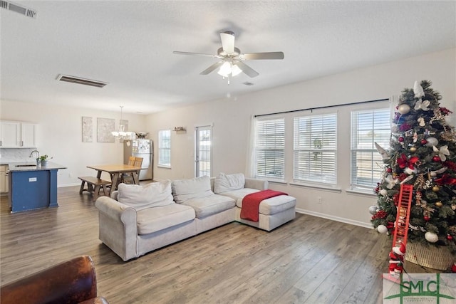 living room with hardwood / wood-style floors, ceiling fan with notable chandelier, a wealth of natural light, and sink