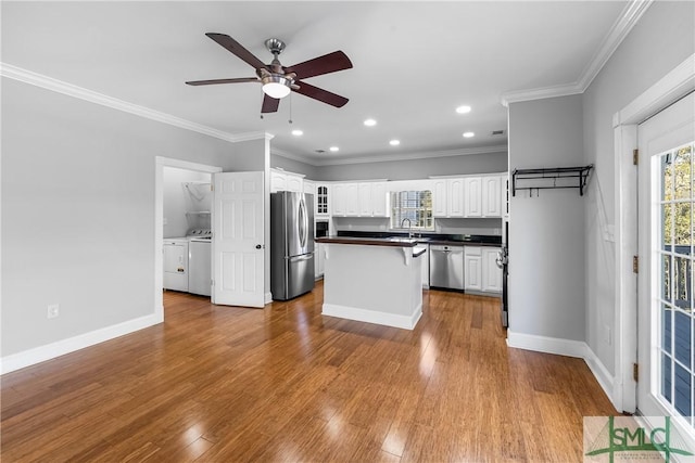 kitchen featuring appliances with stainless steel finishes, washing machine and dryer, ceiling fan, ornamental molding, and white cabinets