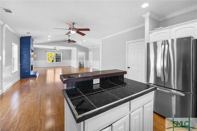 kitchen featuring tile counters, stainless steel refrigerator, a center island, white cabinets, and lofted ceiling