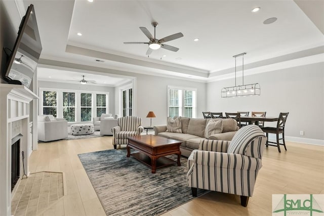 living room with a raised ceiling, ceiling fan, and light wood-type flooring