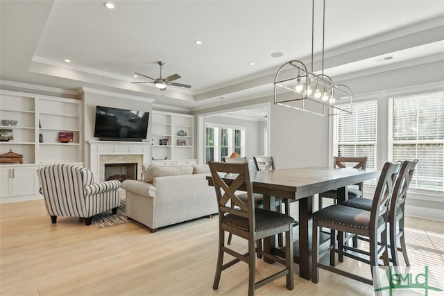 dining area featuring ornamental molding, ceiling fan with notable chandelier, a tray ceiling, and light hardwood / wood-style floors