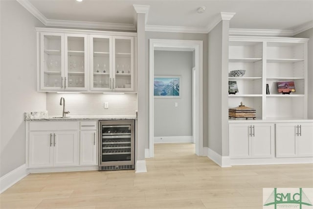 bar with wine cooler, white cabinetry, sink, and light stone countertops