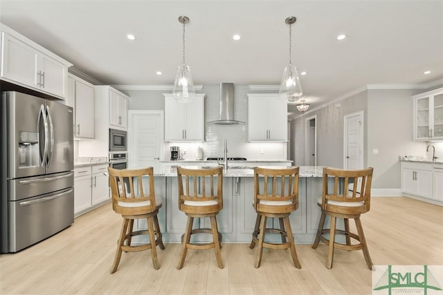 kitchen with white cabinets, wall chimney range hood, light stone countertops, decorative light fixtures, and stainless steel appliances