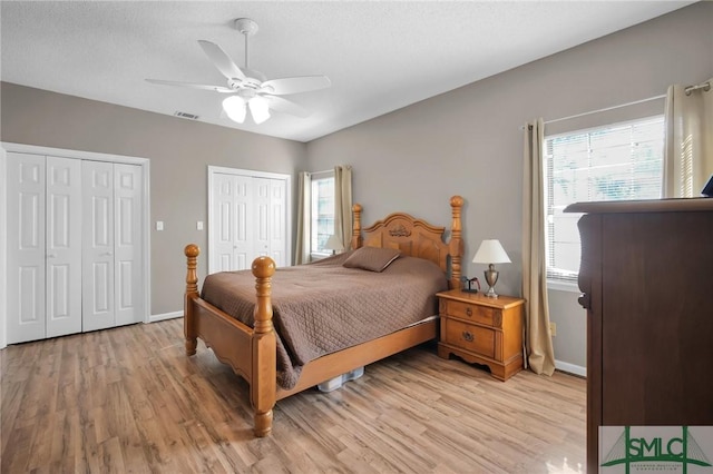 bedroom featuring ceiling fan, multiple windows, light hardwood / wood-style flooring, and two closets