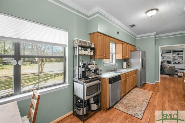 kitchen with crown molding, sink, light wood-type flooring, and stainless steel appliances