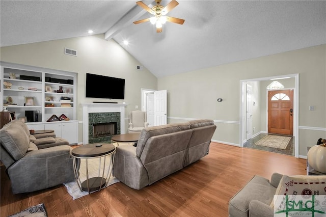 living room featuring ceiling fan, vaulted ceiling with beams, built in features, light hardwood / wood-style flooring, and a textured ceiling