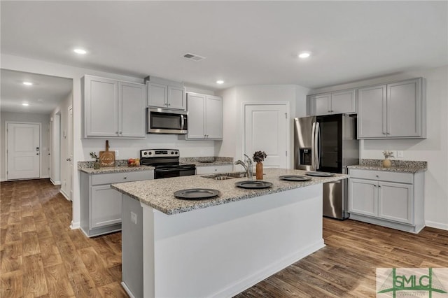 kitchen featuring sink, light stone countertops, light wood-type flooring, an island with sink, and appliances with stainless steel finishes