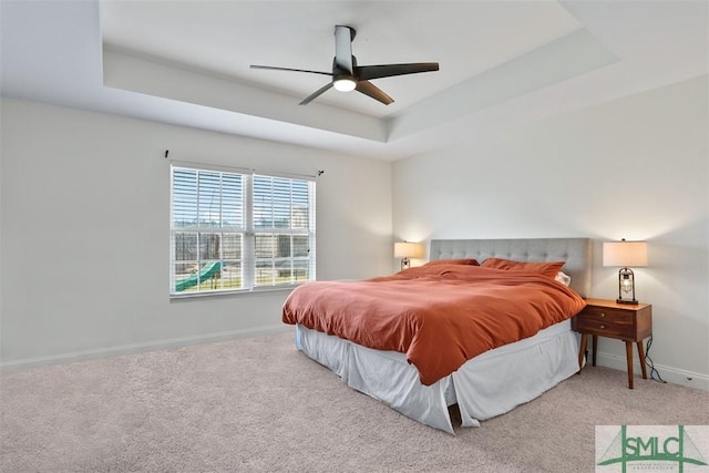 carpeted bedroom with ceiling fan and a raised ceiling