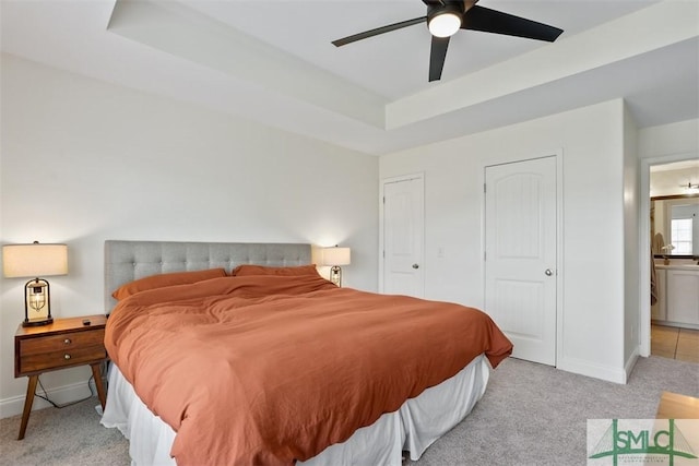 bedroom featuring light colored carpet, a raised ceiling, ceiling fan, and ensuite bathroom