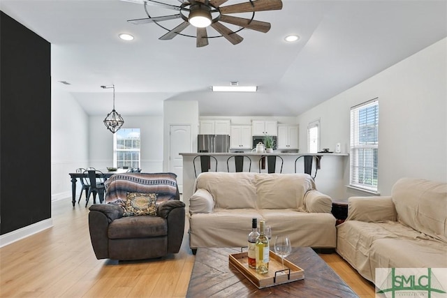 living room with ceiling fan with notable chandelier, light hardwood / wood-style floors, and lofted ceiling